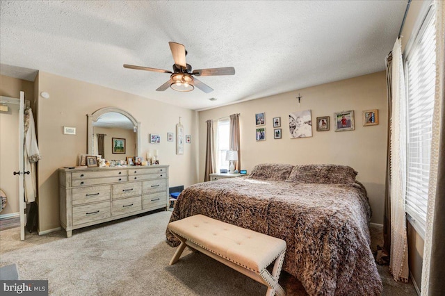 bedroom with a textured ceiling, light colored carpet, ceiling fan, and multiple windows