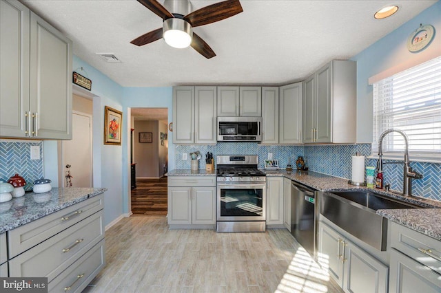 kitchen featuring appliances with stainless steel finishes, light hardwood / wood-style flooring, light stone counters, and sink