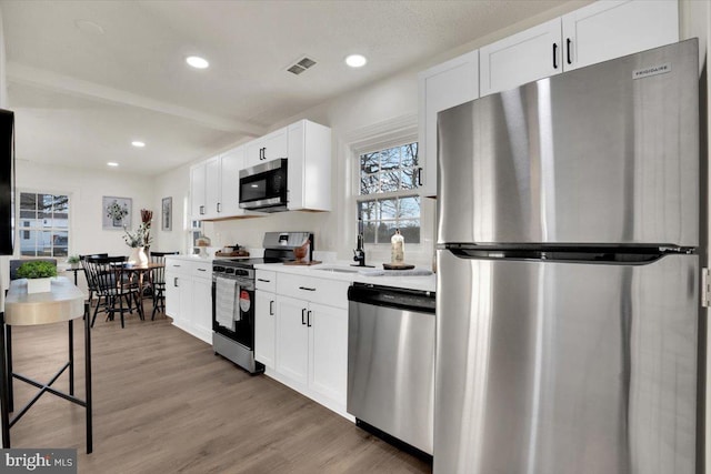 kitchen featuring sink, white cabinets, beamed ceiling, hardwood / wood-style floors, and appliances with stainless steel finishes