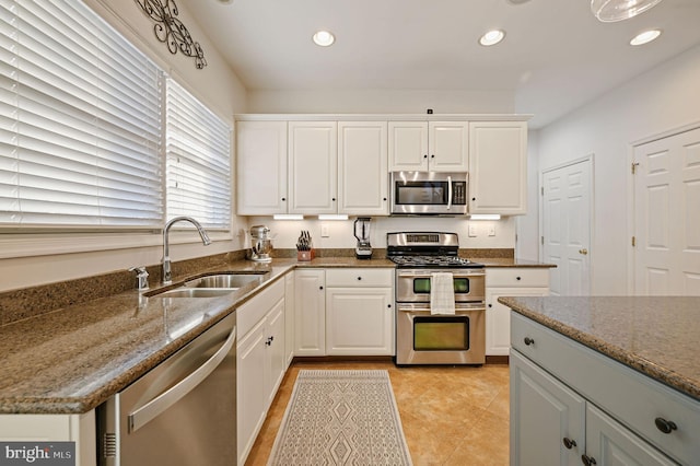 kitchen with stainless steel appliances, dark stone countertops, white cabinets, light tile patterned flooring, and sink