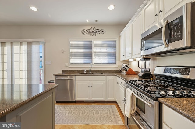 kitchen with sink, dark stone counters, appliances with stainless steel finishes, and white cabinetry