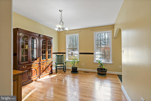 living area featuring light wood-style floors, baseboards, arched walkways, and a notable chandelier