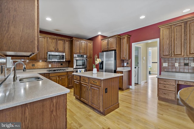 kitchen featuring light wood finished floors, decorative backsplash, a center island, stainless steel appliances, and a sink