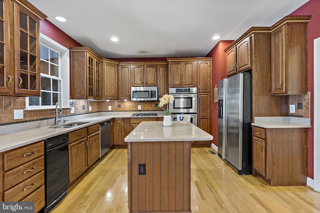 kitchen with decorative backsplash, appliances with stainless steel finishes, light wood-style floors, a sink, and a kitchen island