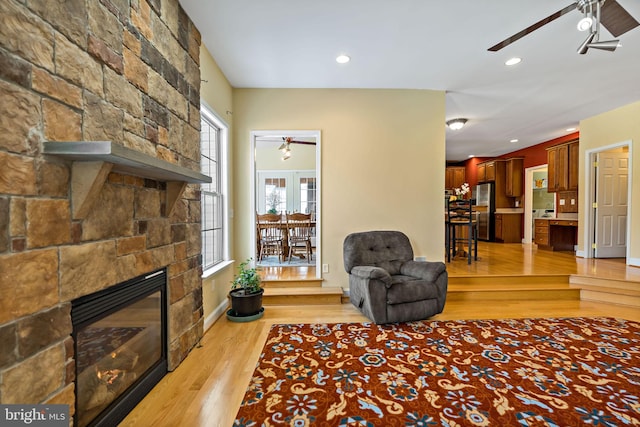 living room featuring baseboards, a ceiling fan, light wood-style flooring, a fireplace, and recessed lighting