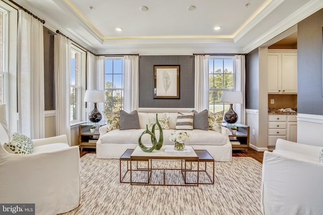 living area with a raised ceiling, light wood-type flooring, and ornamental molding