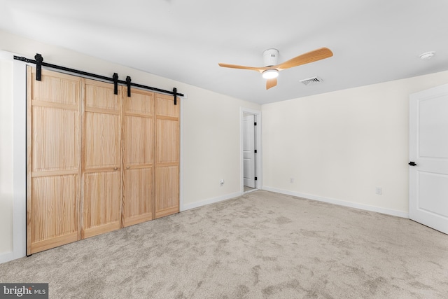 unfurnished bedroom featuring carpet floors, a closet, ceiling fan, and a barn door