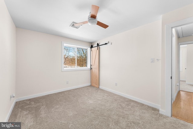 unfurnished bedroom featuring light colored carpet, a barn door, and ceiling fan