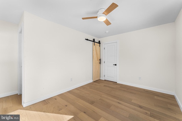 unfurnished bedroom featuring a barn door, ceiling fan, and light hardwood / wood-style flooring