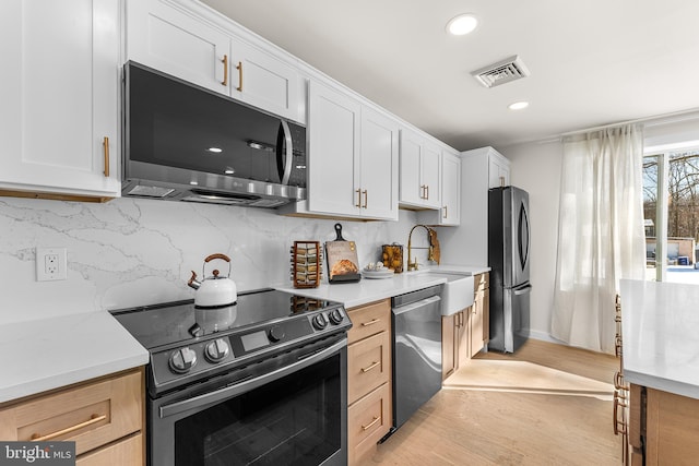 kitchen with tasteful backsplash, appliances with stainless steel finishes, light hardwood / wood-style floors, and white cabinets