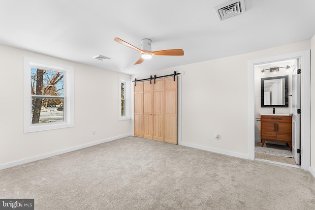 unfurnished bedroom featuring a barn door, connected bathroom, carpet flooring, and multiple windows