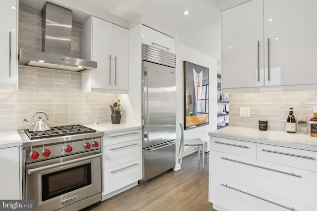 kitchen featuring white cabinetry, light hardwood / wood-style floors, backsplash, wall chimney range hood, and high quality appliances