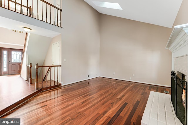 unfurnished living room with high vaulted ceiling, hardwood / wood-style floors, a fireplace, and a skylight