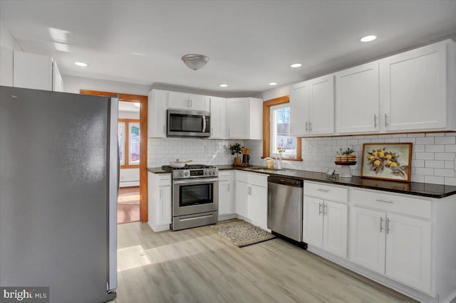 kitchen with tasteful backsplash, appliances with stainless steel finishes, light wood-type flooring, white cabinets, and sink