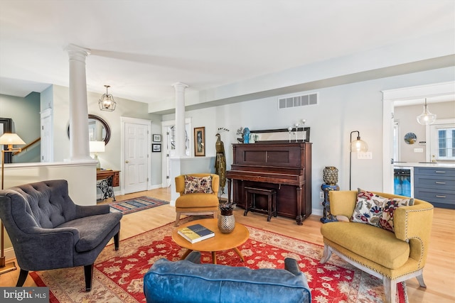 living room with wine cooler, decorative columns, and light hardwood / wood-style flooring