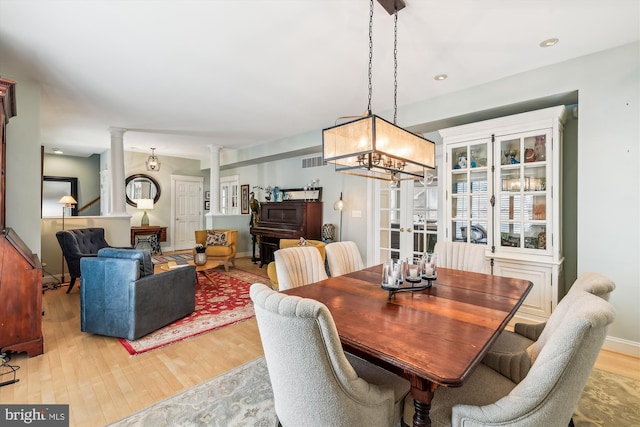 dining area with a notable chandelier, light hardwood / wood-style floors, and ornate columns