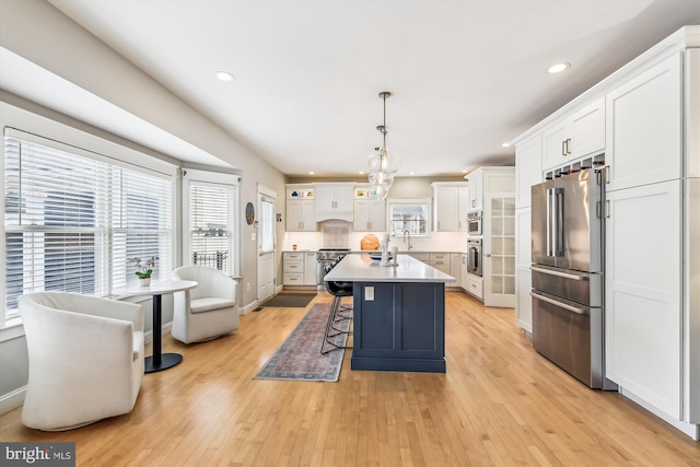 kitchen with white cabinetry, decorative light fixtures, a center island with sink, and premium appliances