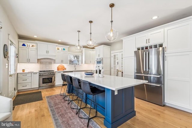 kitchen with a kitchen island, a breakfast bar, white cabinets, hanging light fixtures, and stainless steel appliances