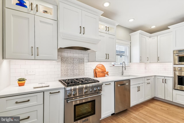 kitchen with sink, stainless steel appliances, tasteful backsplash, white cabinets, and light wood-type flooring