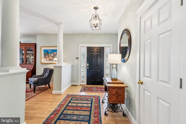 entryway with a notable chandelier, light hardwood / wood-style floors, and ornate columns