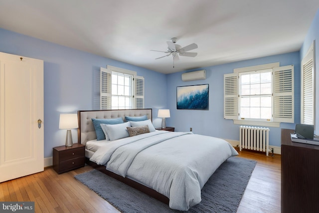 bedroom with a wall mounted air conditioner, ceiling fan, radiator, and light hardwood / wood-style floors