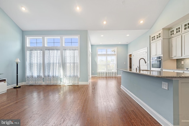 kitchen featuring dark hardwood / wood-style floors, oven, decorative backsplash, dark stone counters, and sink