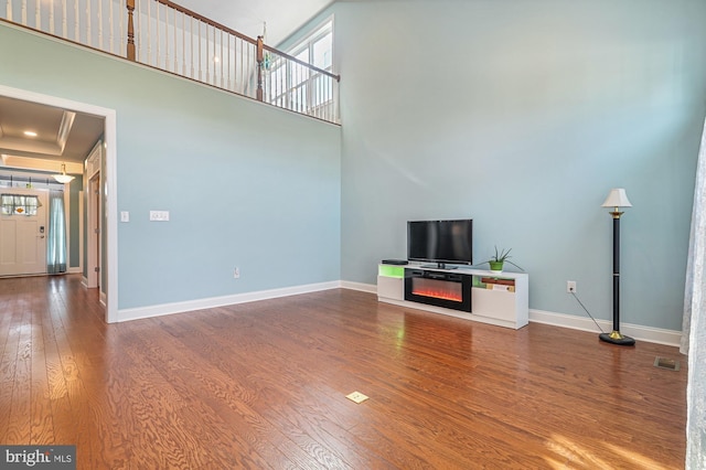 unfurnished living room featuring a towering ceiling, hardwood / wood-style flooring, and a raised ceiling