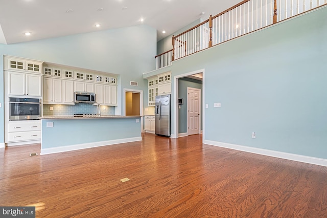 kitchen with stainless steel appliances, tasteful backsplash, high vaulted ceiling, dark hardwood / wood-style flooring, and a kitchen island with sink