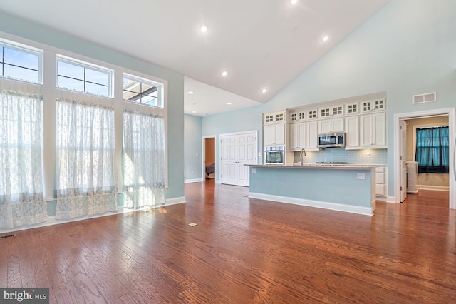 kitchen with high vaulted ceiling, appliances with stainless steel finishes, a kitchen island with sink, and decorative backsplash