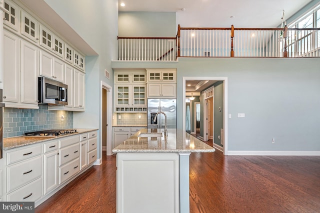 kitchen featuring a high ceiling, decorative backsplash, a kitchen island with sink, appliances with stainless steel finishes, and sink