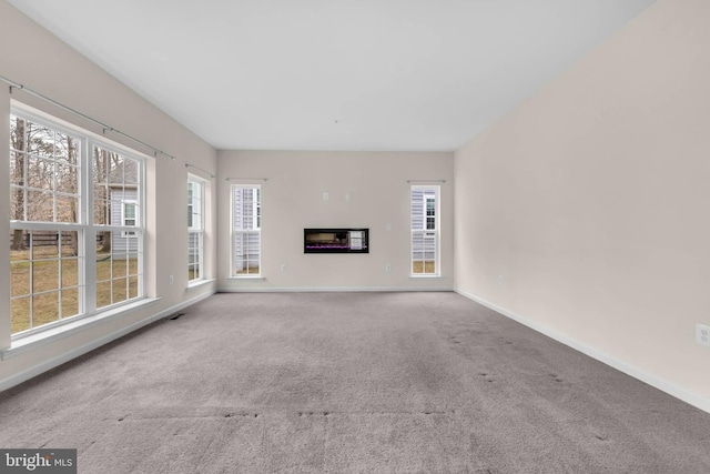 unfurnished living room featuring baseboards, carpet flooring, and a glass covered fireplace