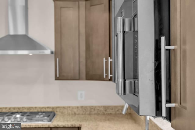 interior space with stainless steel gas cooktop, wall chimney exhaust hood, and light stone countertops