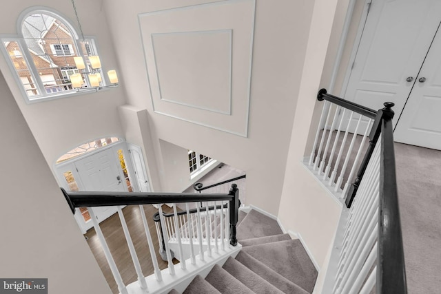 stairs with a chandelier, carpet floors, a towering ceiling, and baseboards