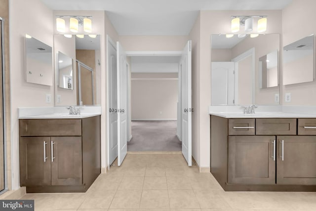 bathroom featuring a stall shower, baseboards, two vanities, tile patterned flooring, and a sink