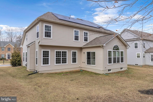 rear view of house featuring a shingled roof, roof mounted solar panels, and a lawn