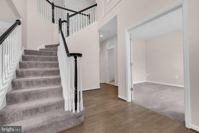 stairs with a high ceiling, visible vents, baseboards, and wood finished floors