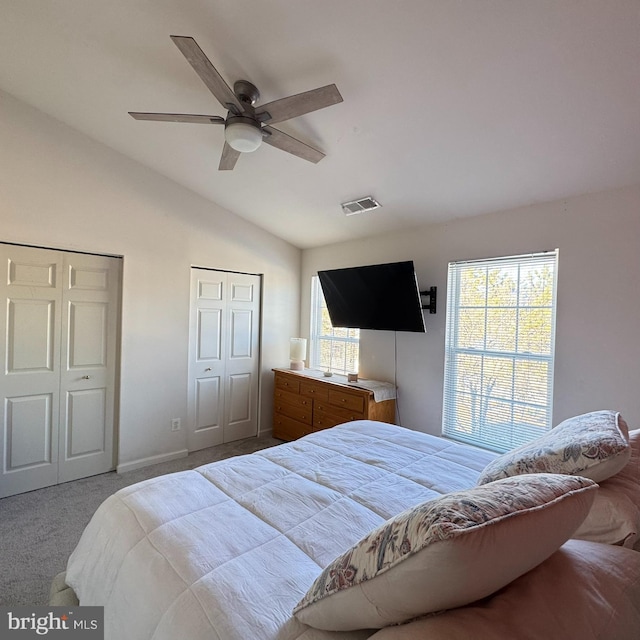 carpeted bedroom with ceiling fan, two closets, multiple windows, and lofted ceiling