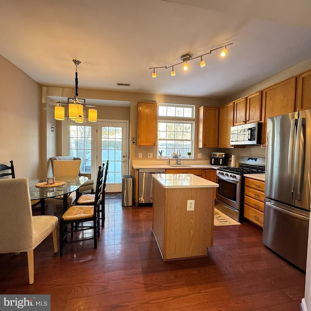 kitchen with appliances with stainless steel finishes, hanging light fixtures, a center island, dark wood-type flooring, and sink