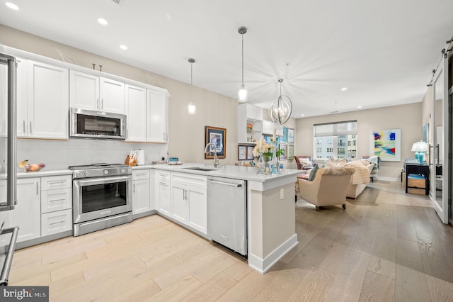 kitchen with white cabinets, appliances with stainless steel finishes, sink, hanging light fixtures, and kitchen peninsula