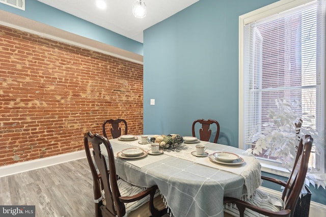 dining room with brick wall and wood-type flooring