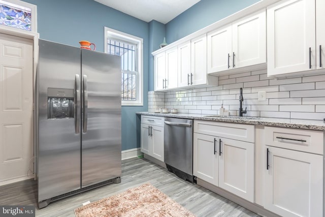 kitchen with light stone countertops, backsplash, white cabinetry, appliances with stainless steel finishes, and sink