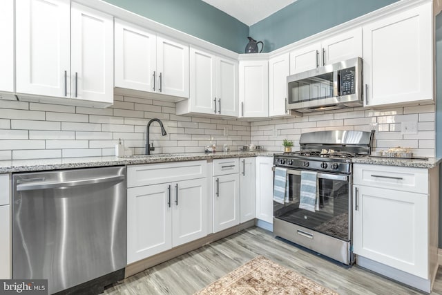 kitchen with white cabinets, light stone counters, light wood-type flooring, decorative backsplash, and appliances with stainless steel finishes