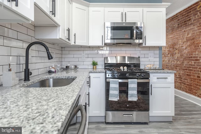 kitchen with appliances with stainless steel finishes, light stone countertops, brick wall, sink, and white cabinetry