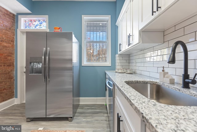 kitchen featuring stainless steel appliances, light stone counters, decorative backsplash, sink, and white cabinetry