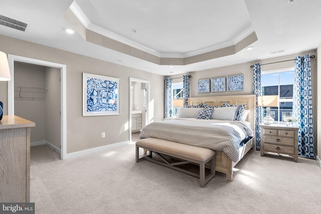 carpeted bedroom featuring a tray ceiling, a walk in closet, ornamental molding, and ensuite bathroom