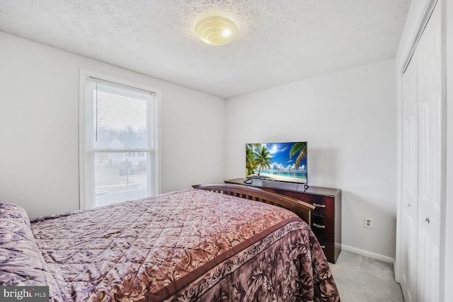 bedroom featuring a textured ceiling, baseboards, a closet, and light colored carpet