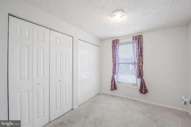 unfurnished bedroom featuring baseboards, visible vents, multiple closets, and light colored carpet