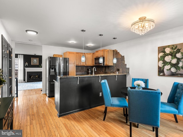 kitchen featuring light hardwood / wood-style floors, stainless steel fridge, kitchen peninsula, decorative backsplash, and decorative light fixtures