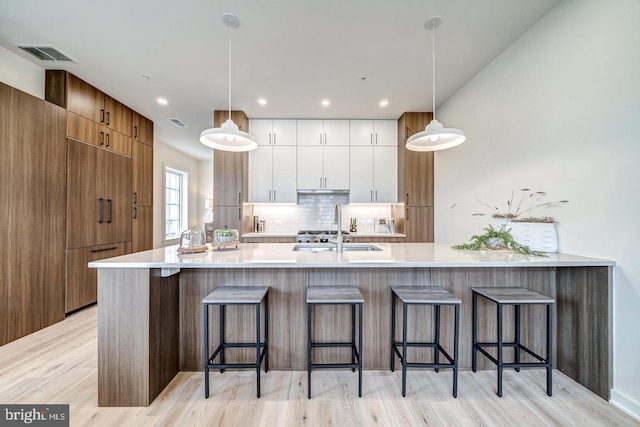 kitchen with decorative light fixtures, backsplash, white cabinets, and light hardwood / wood-style floors