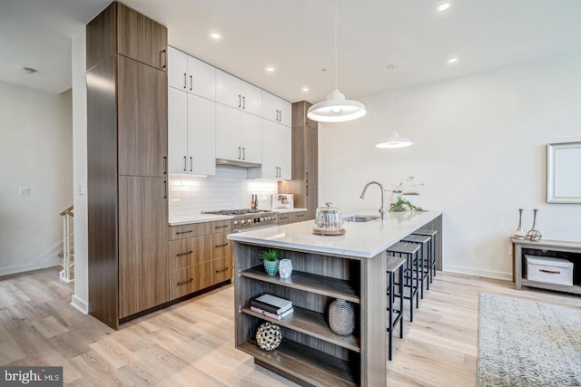 kitchen with light hardwood / wood-style floors, hanging light fixtures, an island with sink, white cabinets, and sink